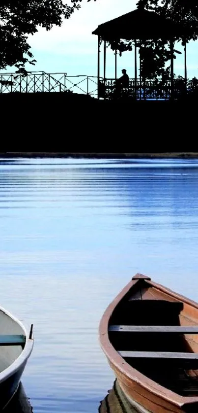 Tranquil lakefront with two boats and a gazebo under a blue sky.