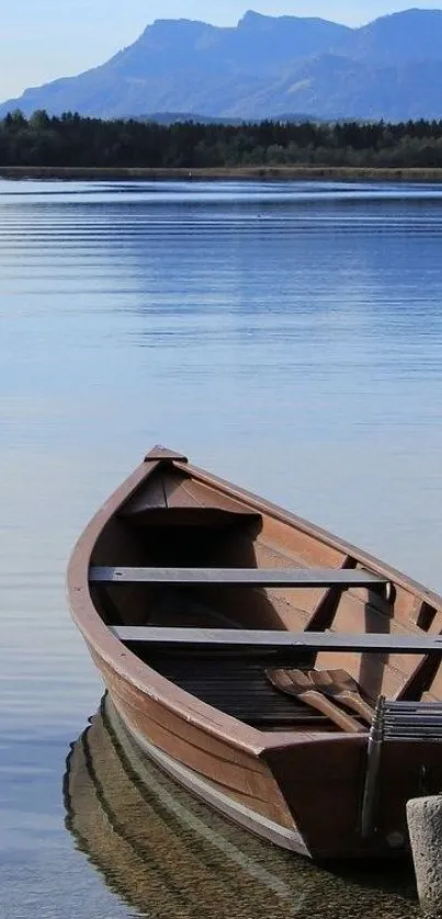 Wooden boat on a peaceful lake with mountains in the background under blue sky.