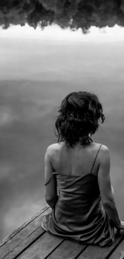 Black and white image of a woman by a calm lake, viewed from behind.