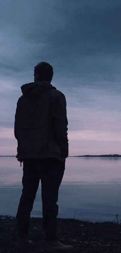 Silhouette of person by a calm lake at dusk.