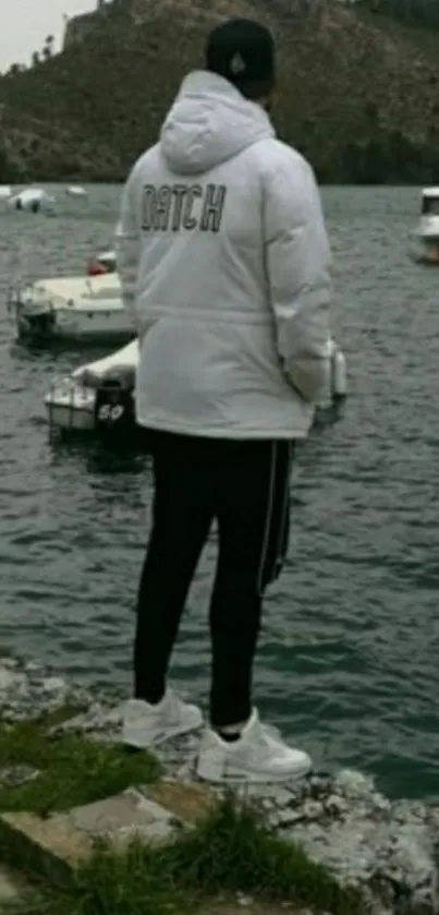 Person in white jacket by a serene lakeside with boats.