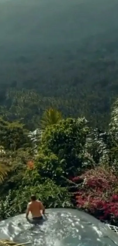 Man sitting by an infinity pool with lush green landscape.