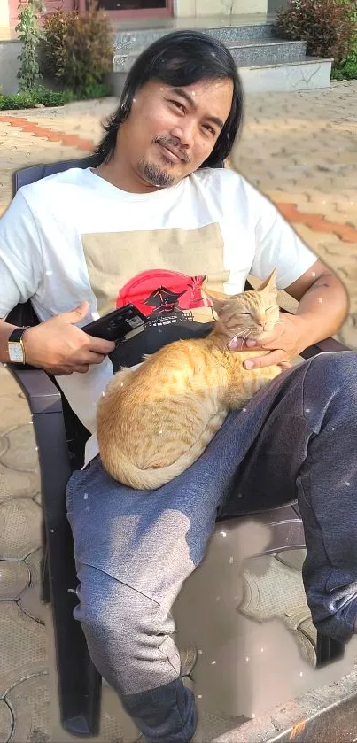 A man comfortably seated with a cat on his lap outdoors.