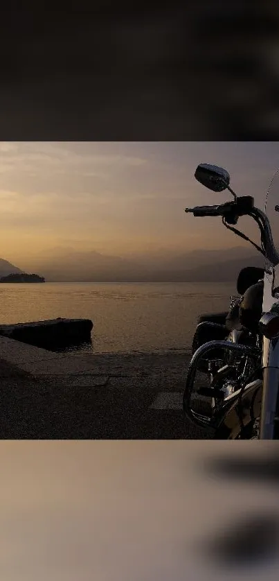 Motorcycle parked by the sea at sunset with mountains in the background.