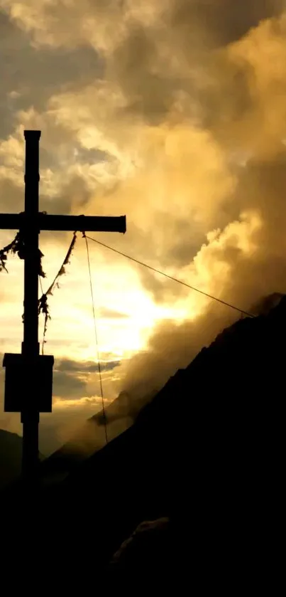 Silhouette of a mountain cross at sunset with orange and yellow hues.