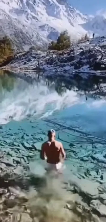 Man wading into azure lake beneath snowy mountains.