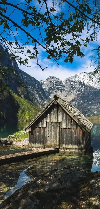 Rustic cabin by a tranquil mountain lake with snowy peaks.