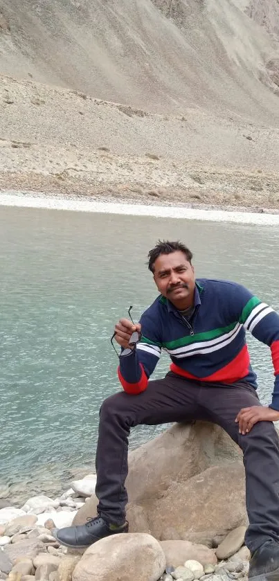 A man sitting by a serene mountain lake with rocky surroundings.