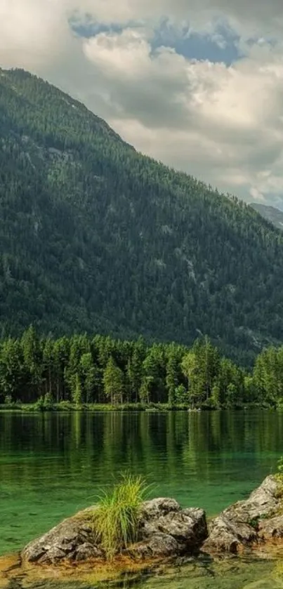 Serene mountain lake with lush green forest and clear waters under a cloudy sky.