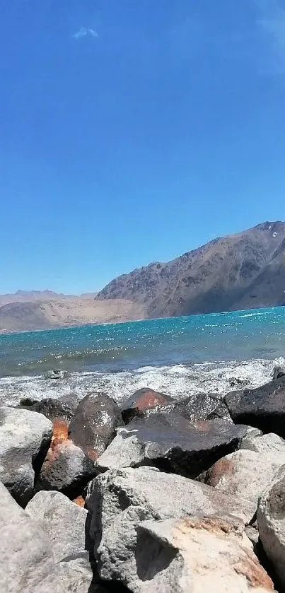 Serene mountain lake with rocky shoreline under a clear blue sky.