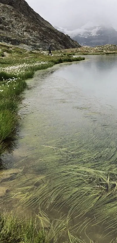 Serene mountain lake with green grass and foggy peaks in the background.