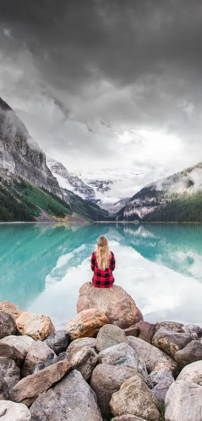 Girl sitting by a tranquil mountain lake with a cloudy sky.