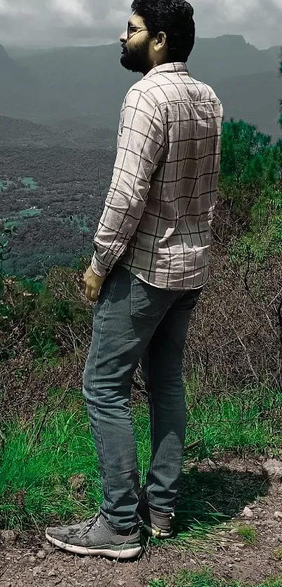 Man enjoying a serene mountain view with lush greenery and misty skies.