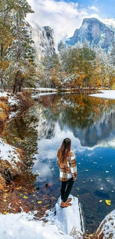 Woman stands by a reflective lake surrounded by snowy mountains.