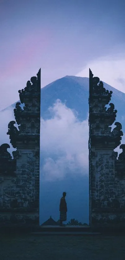 Man standing in temple gate with mountain backdrop at dusk.
