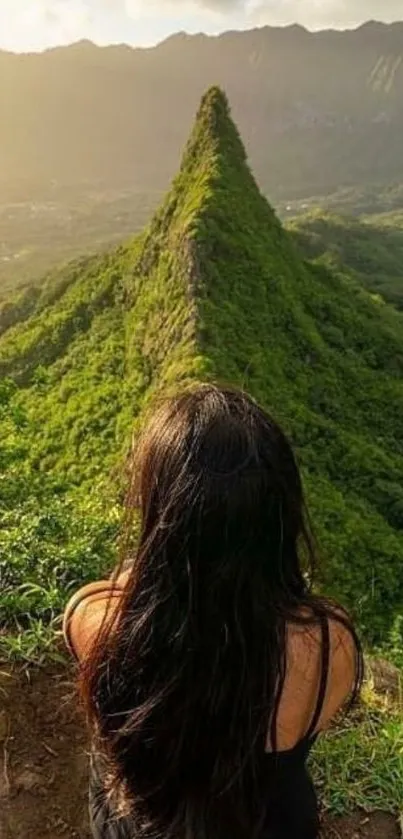 Woman gazing at lush green mountain ridge under a serene sunset.