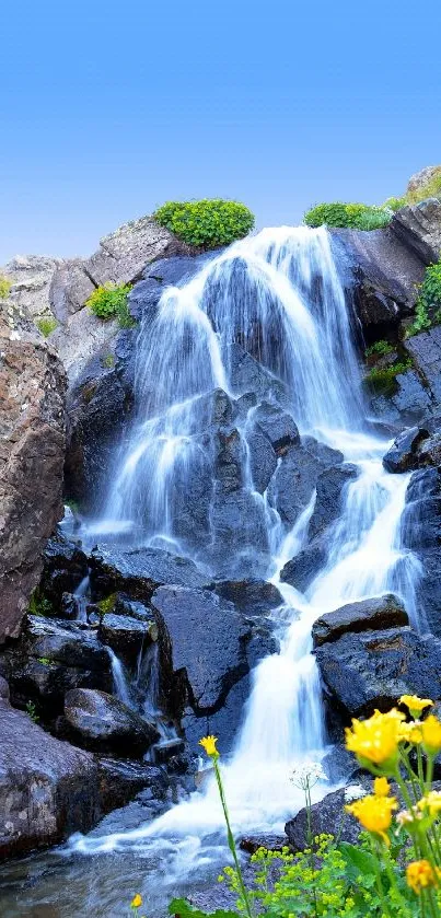 Serene mountain waterfall with vibrant flowers and a clear blue sky.