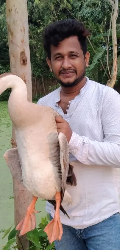 Man holding a goose in a lush, green outdoor setting.