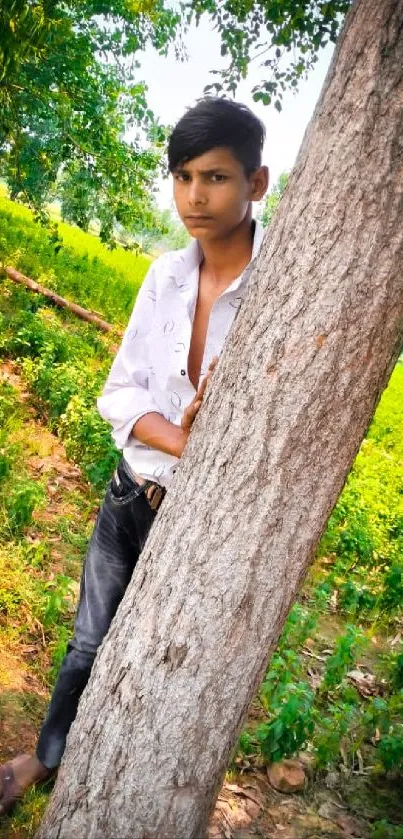 A young man leaning against a tree in a lush green forest.