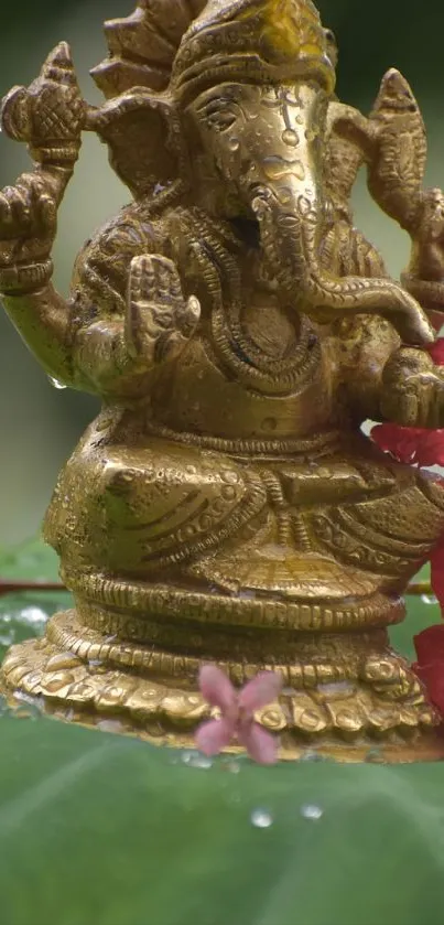 Golden Ganesha idol on green leaves with flowers.