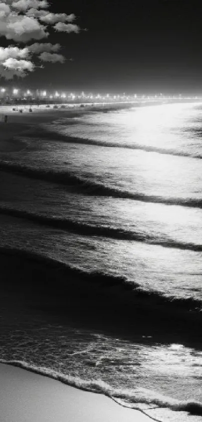 Black and white beach at night with moonlit waves and a tranquil shoreline.