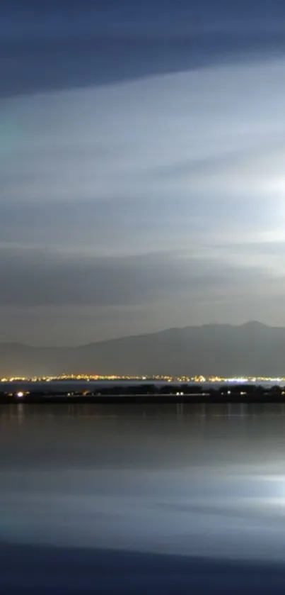 Serene night sky reflecting on a calm lake with lights in the horizon.