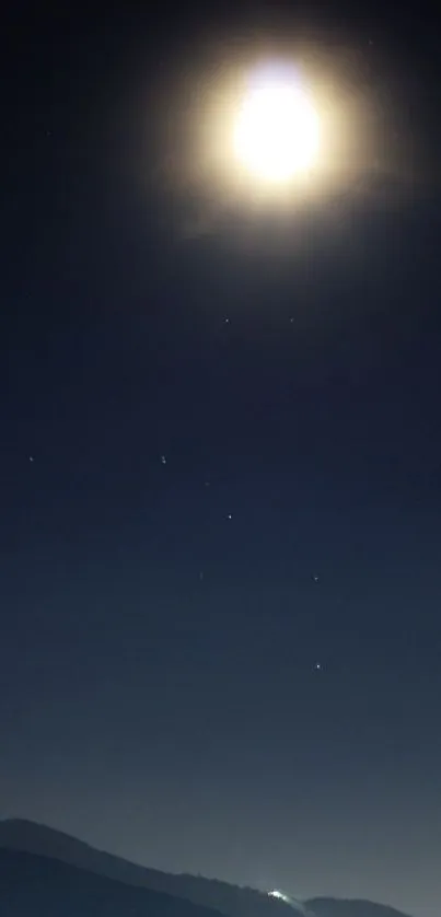 A bright moon illuminates a dark night sky with stars above a silhouetted landscape.