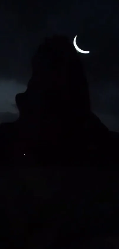 Crescent moon over a dark mountain silhouette at night.