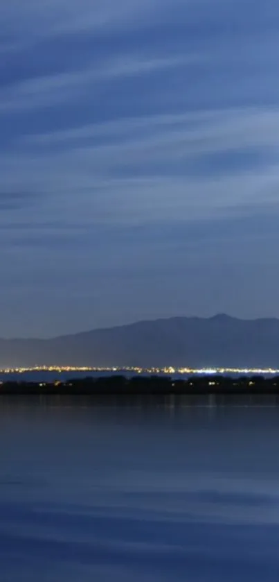 Serene night sky with city lights reflected on a calm blue lake.