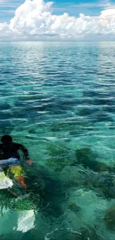 Lone surfer gliding over turquoise ocean under a vast cloudy sky.