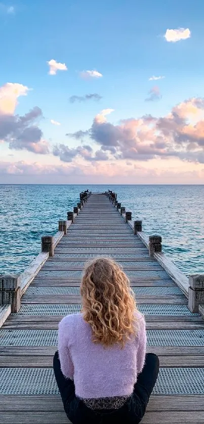 Person sitting on dock overlooking serene ocean and sky.