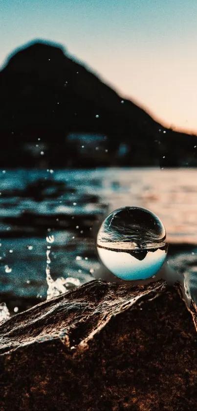 Ocean scene with a glass sphere reflecting the sunset and mountain.