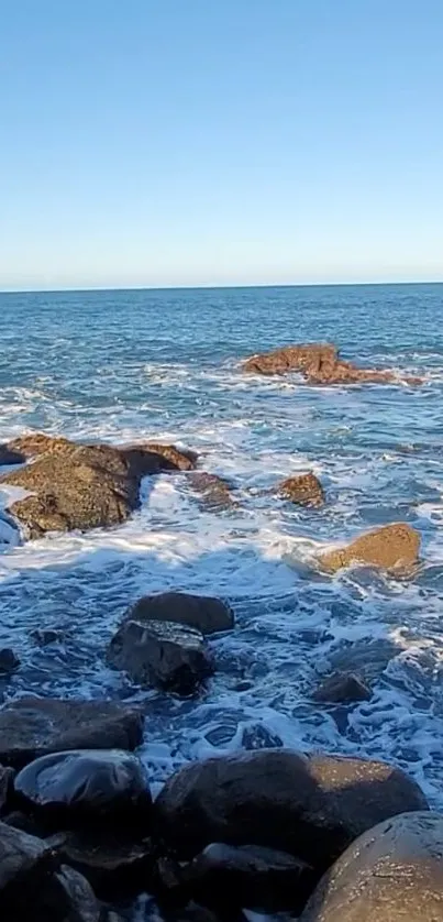 Tranquil ocean with rocks and blue sky wallpaper.