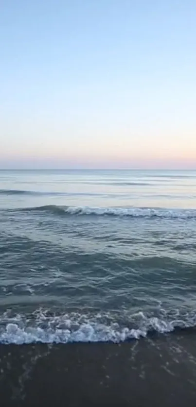 Serene ocean sunset with soft waves and a pastel blue sky.