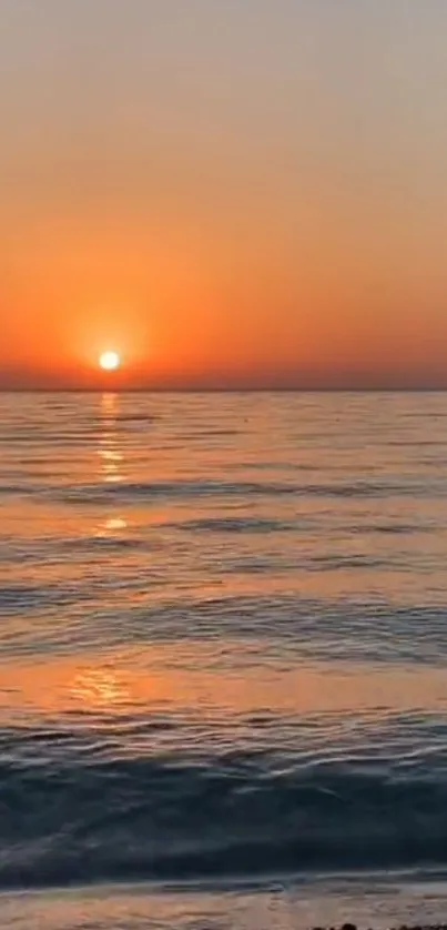 Serene sunset over ocean with orange sky and reflection.