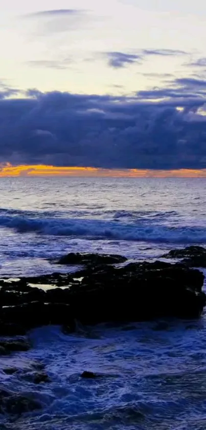 Serene ocean sunset with waves and a rocky shore, under a cloudy sky.