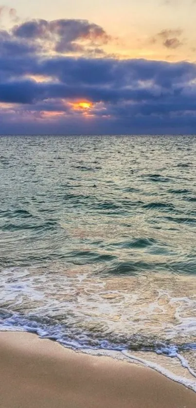 Serene ocean sunset with waves gently lapping the sandy beach under a colorful sky.