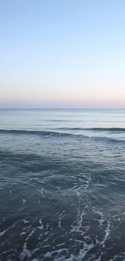 Serene ocean sunset with blue waves and pastel sky.