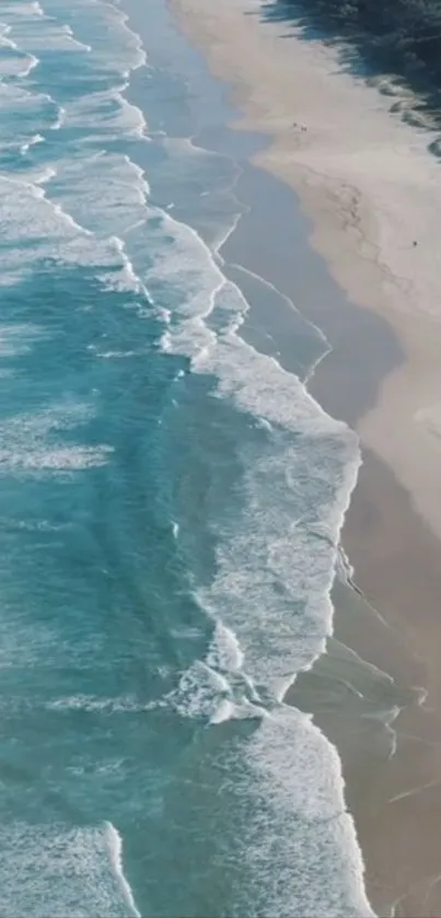 Aerial view of turquoise ocean waves gently hitting the sandy beach shore.