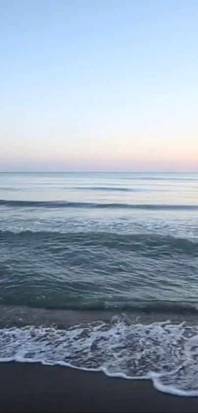 Peaceful ocean waves and sunrise sky over a sandy beach.