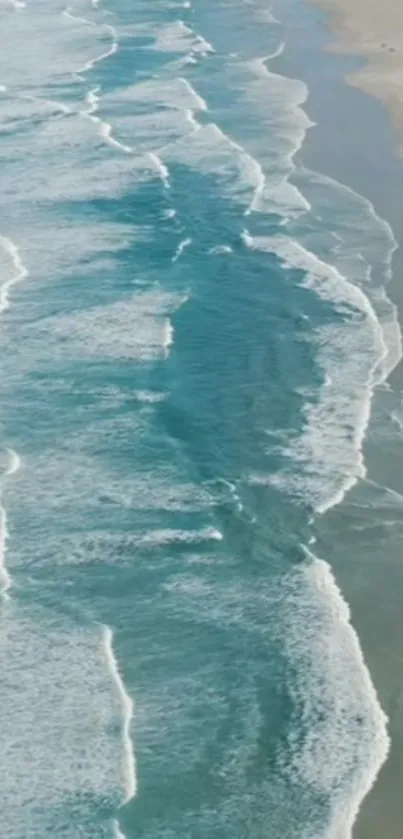 Aerial view of turquoise ocean waves gently hitting a sandy beach.