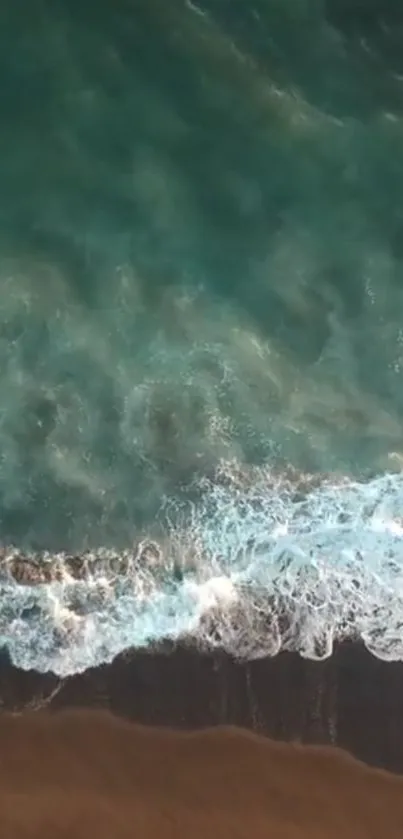 Aerial view of teal ocean waves meeting the dark sandy shore.