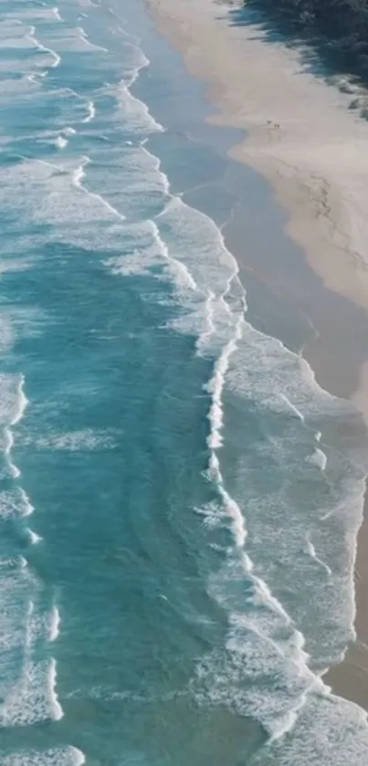 Aerial view of serene ocean waves meeting a sandy shore under clear skies.