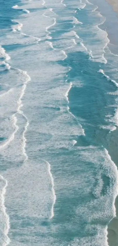 Aerial view of light blue ocean waves on a sandy beach.