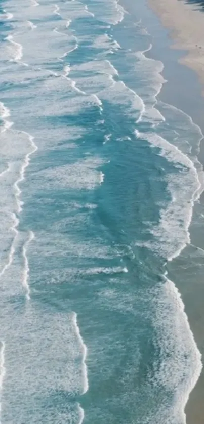 Aerial view of blue ocean waves gently washing against a sandy shore.