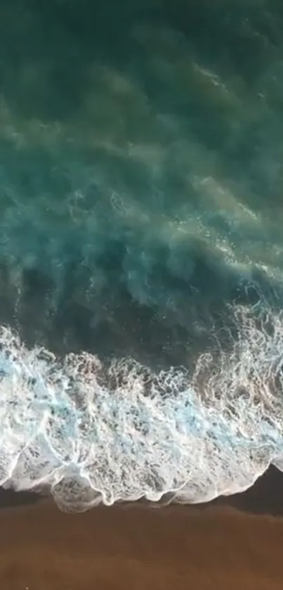 Aerial view of ocean waves meeting a sandy beach with teal water.