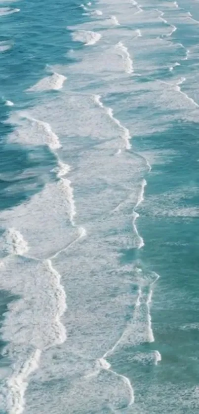 Aerial view of gentle ocean waves with turquoise water on a sandy beach.