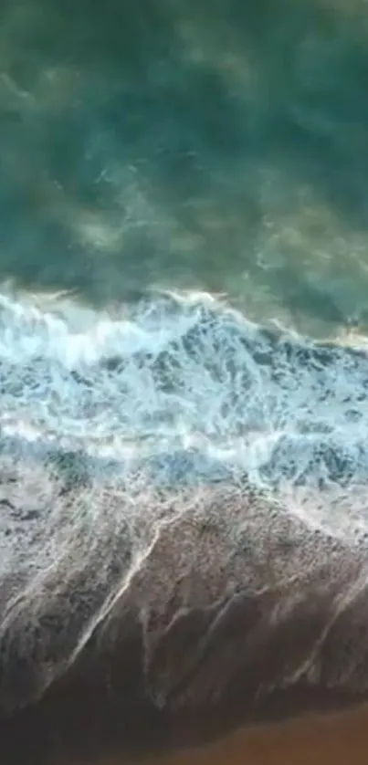 Aerial view of ocean waves crashing on a beach, showcasing teal water and white foam.