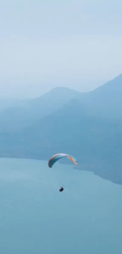 Paraglider gliding over calm, blue waters and mountains.