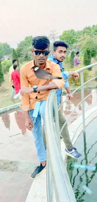 Two men standing on a bridge with water and greenery in the background.